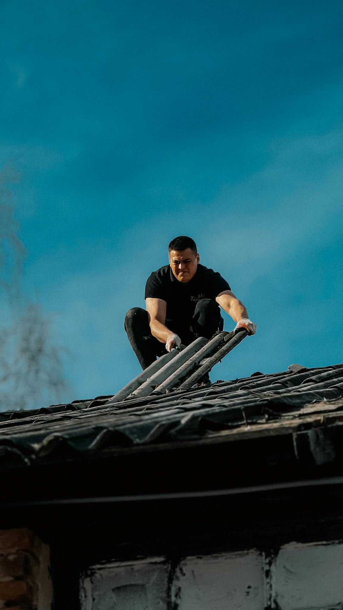 A man climbs a ladder onto a rooftop under a clear blue sky, focusing on safety and construction.