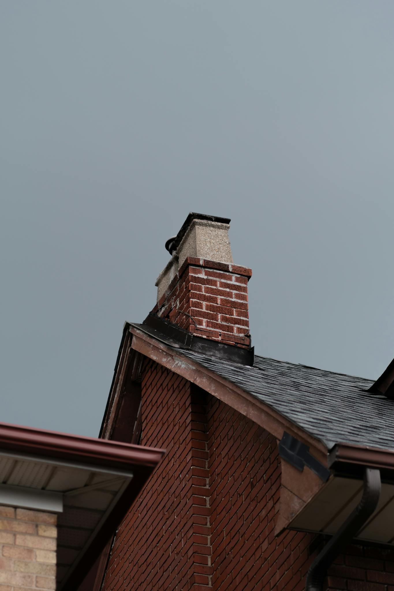 Detailed view of a brick chimney on a residential roof under a cloudy sky.